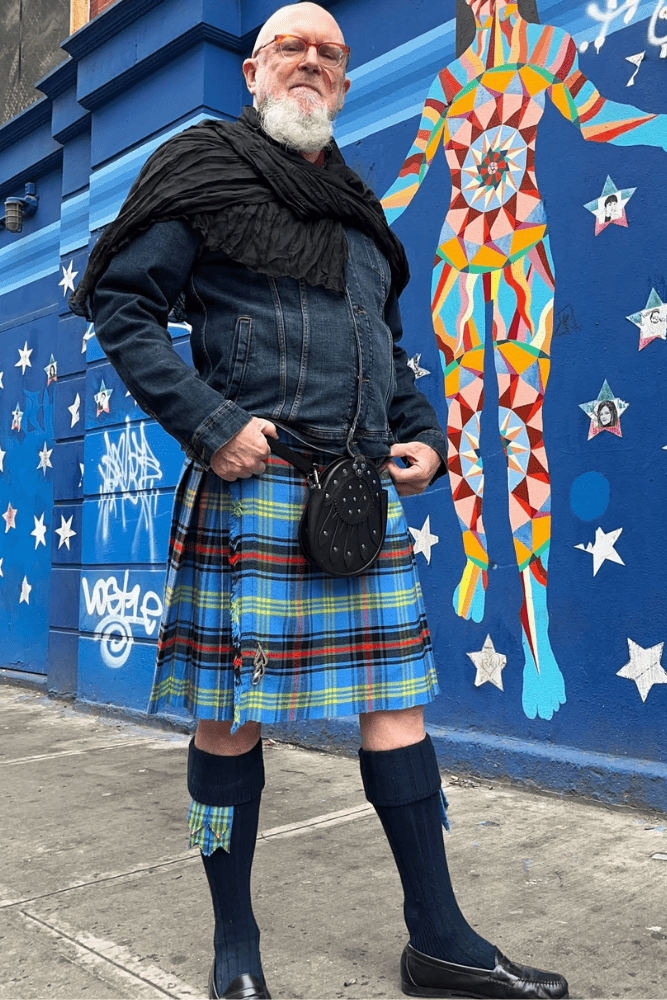 Person wearing a kilt standing in front of a colorful mural on a blue wall.
