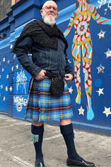 Person wearing a kilt standing in front of a colorful mural on a blue wall.